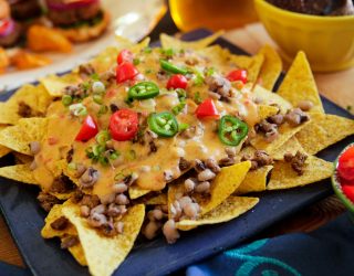 close up of black eye peas nachos inclusing tortilla chips, queso, red and green peppers and cillantro on top