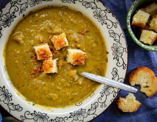 a bowl of green split pea and ham soup with croutons in it and a side of bread