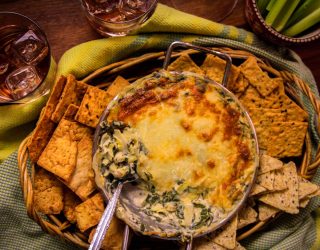 a bowl of spinach artichoke white bean dip surrounded by various bread and crackers