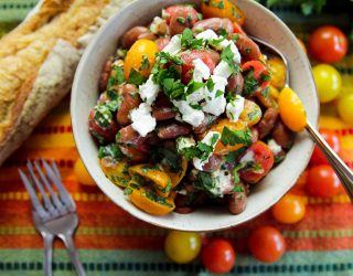 Bowl of Red Bean Red Bean & Goat Cheese Mediterranean Salad with fresh, whole cherry tomatoes, and french bread on the side