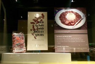 a display at the smithsonian showing a package of camellia brand red beans, some images and a picture of a plate of red beans and rice