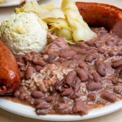 a close up of a plate of red beans and rice with a side of mashed potatoes, 2 sausage links, and some chips from mother's restaurant