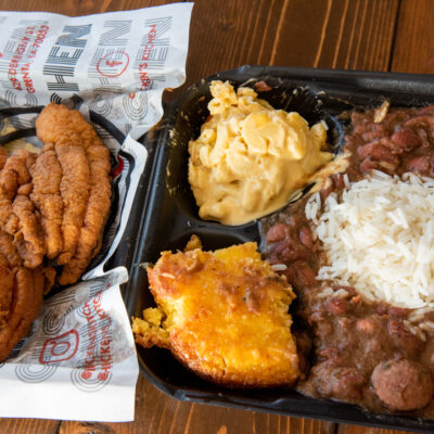 a top down view of a to go box full of red beans and rice with a side of corn bread, mac and cheese and fried chicken