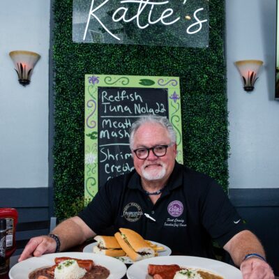 chef standing infront of sign at Katie's resturant posing with 2 plates of red beans and rice