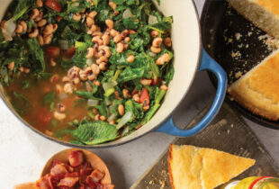 overhead image of large pot of cooked greens and blackeyed peas surrounded by cornbread on the table