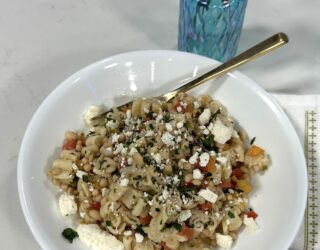 white bowl of cooked lady cream cavier pasta salad on light colored table with blue vase behind it and red flowers in vase