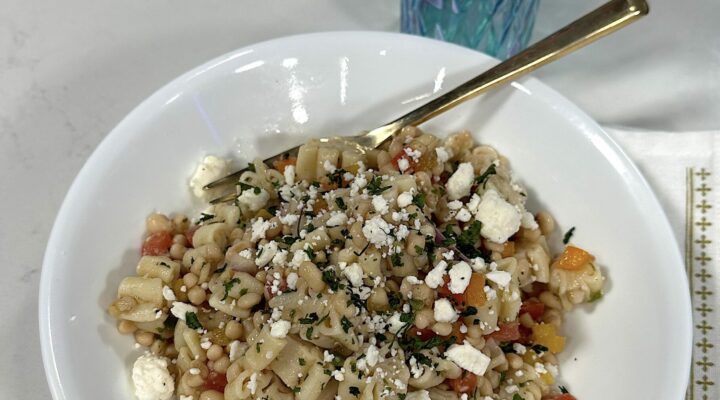 white bowl of cooked lady cream cavier pasta salad on light colored table with blue vase behind it and red flowers in vase