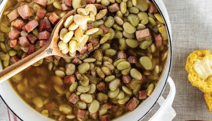 overhead image of large, white, stovetop pot on white table with white and red cloth napkin underneath and cooked butter beans inside pot