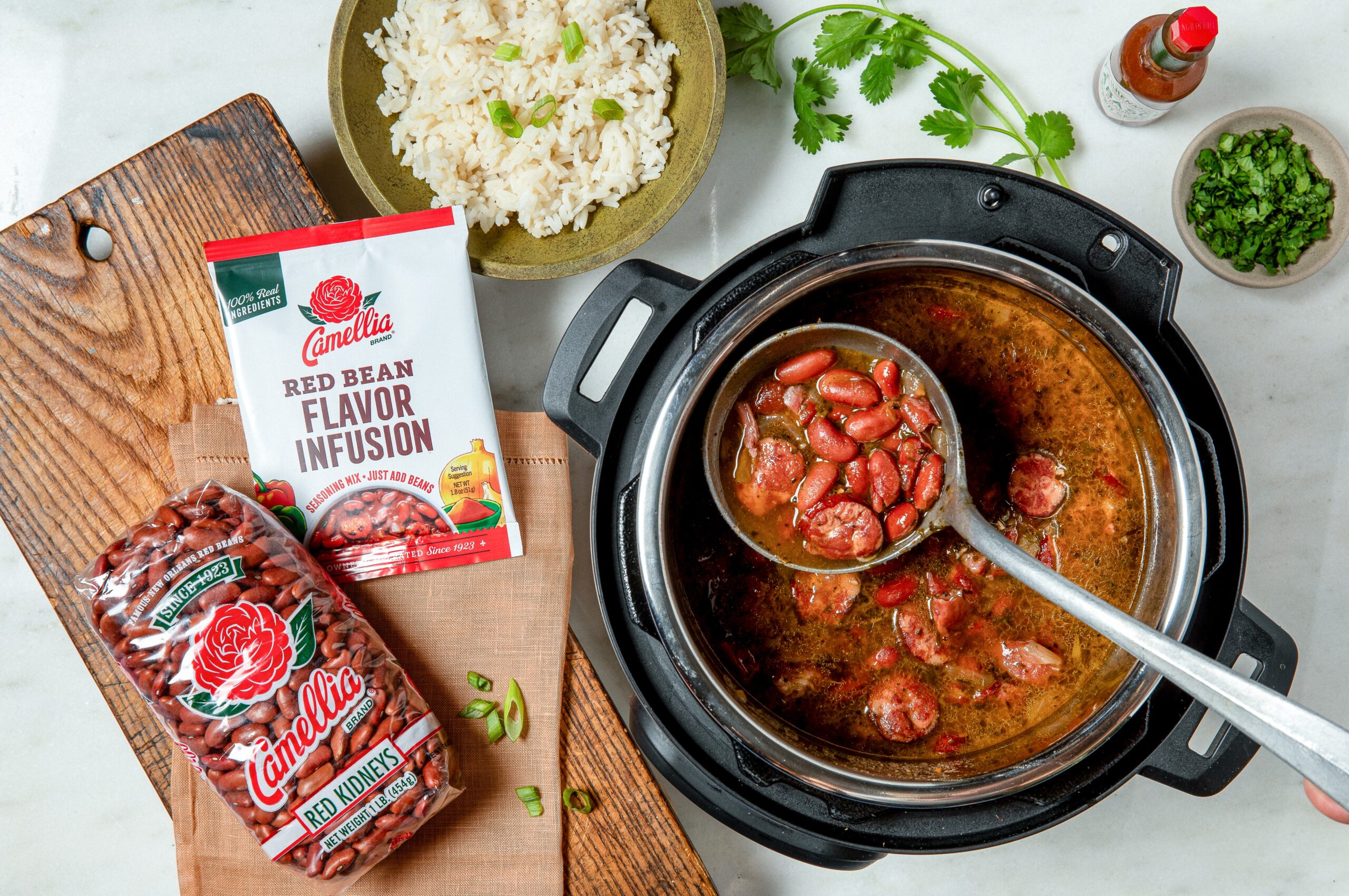 overhead image of Instant Pot full of cooked Instant Pot Red Bean Soup, with bag of Red Kidney beans and Flavor Infusion pouch laying next to it on a wooden cutting board.