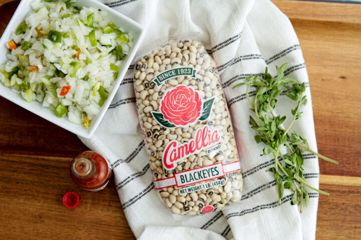 Dried Blackeye peas in Camellia packaging on a kitchen towel next to a white bowl of chopped seasonings